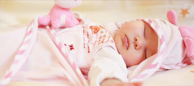 A baby is sleeping in her crib with pink and white blankets.