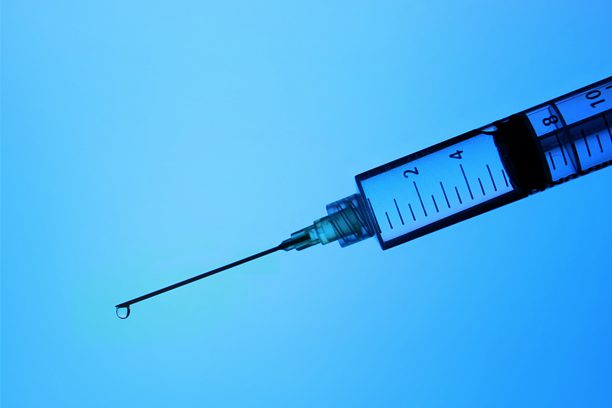 A needle with a syringe in it is shown against the sky.