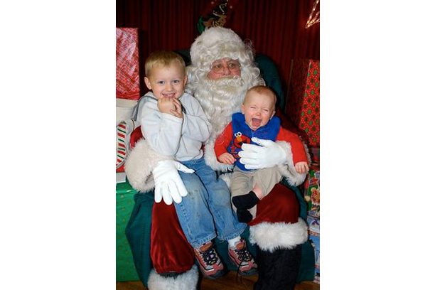 A man sitting on top of santa 's lap with two children.
