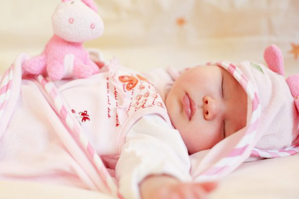 A baby is sleeping in her crib with a stuffed animal.