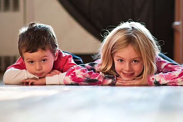 Two children laying on the floor looking at a camera.